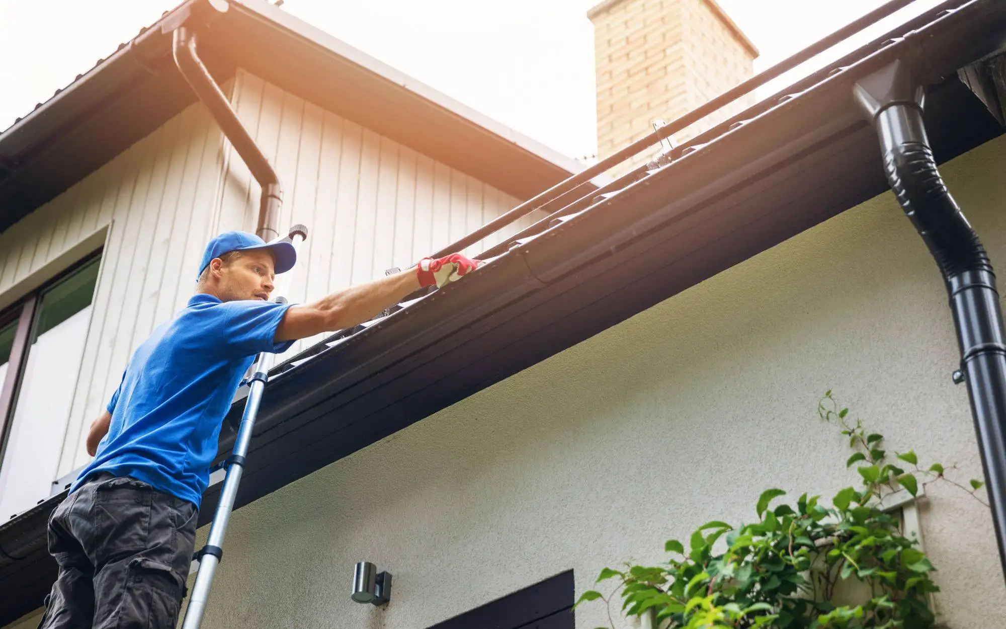 Man On Ladder Cleaning House Gutter From Leaves And Dirt